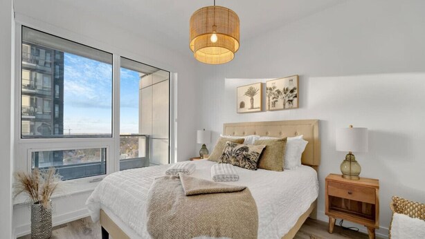 Een slaapkamer met een groot bed, nachtkastjes, een hanglamp en uitzicht op het omliggende landschap.