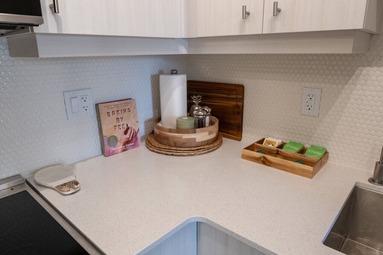 A kitchen with white cabinets, a wooden cutting board, a paper towel holder, a box of baking paper, and a wooden box with green labels.