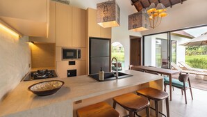 A modern kitchen with a large island, bar stools, and a dining area with a view of the outdoors. - Rocca Bella Villa 2 by Alfred in Bali (Canggu)