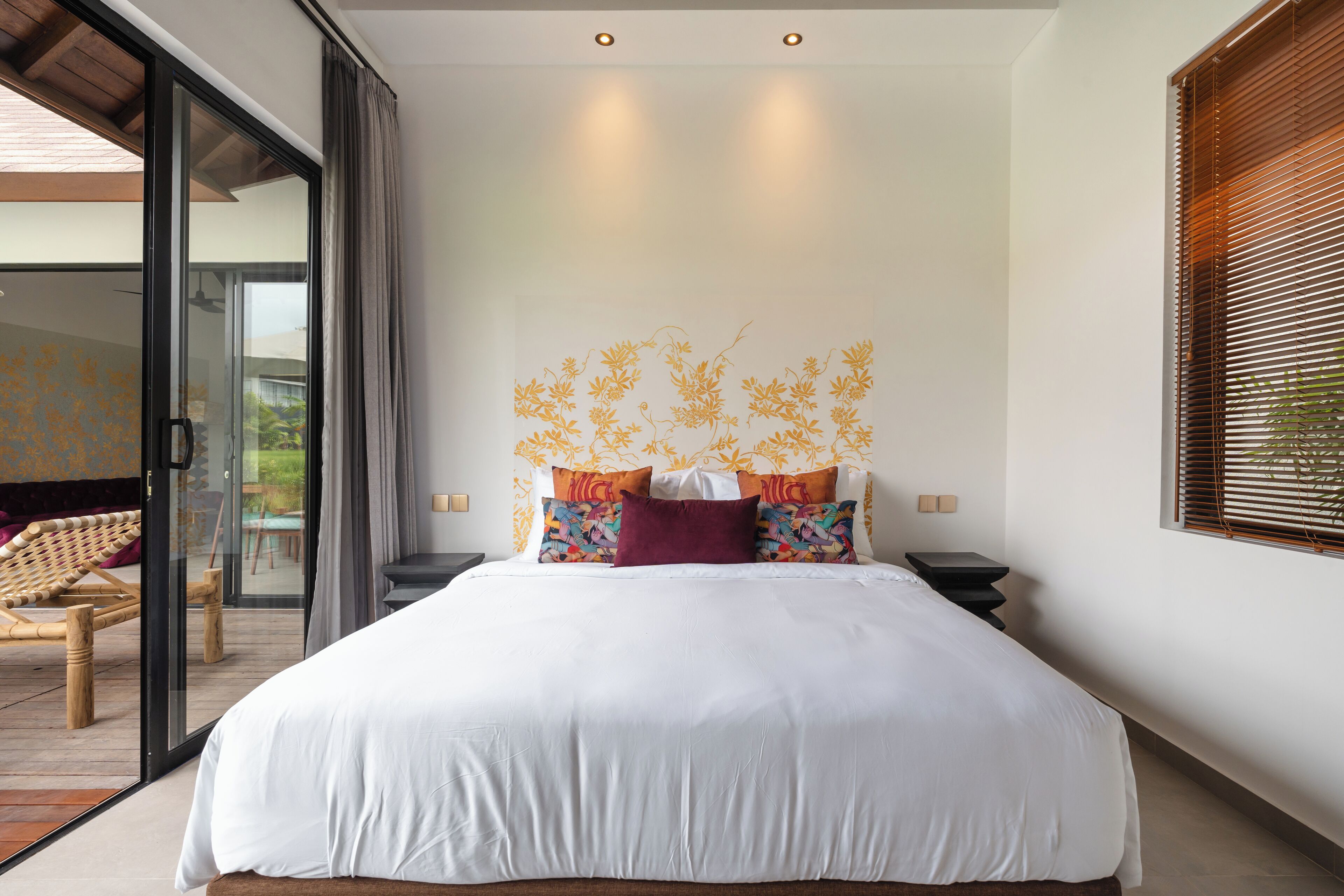 Een moderne slaapkamer met een groot bed, een glazen deur naar een balkon, en een muur met een bloemendesign.