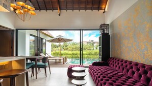 A modern interior with a plush purple sofa, a dining area with a table and chairs, and a view of a swimming pool through large glass doors. - Rocca Bella Villa 2 by Alfred in Bali (Canggu)