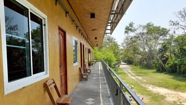 A long corridor with wooden benches and doors, leading to a grassy area with trees. - Jayzada Fang Resort (Fang)
