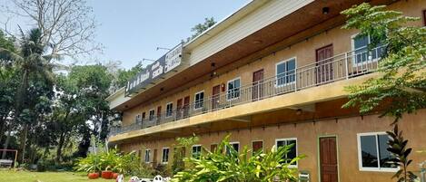 A two-story building with a balcony on the upper floor. There are potted plants and outdoor seating.