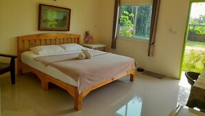 A bedroom with a wooden bed, a bedside table, a nightstand, a window with curtains, and a view of greenery outside. - Jayzada Fang Resort (Fang)