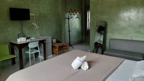 A hotel room with a bed, a desk, a chair, a small table, a television, and a mirror. - Jayzada Fang Resort (Fang)