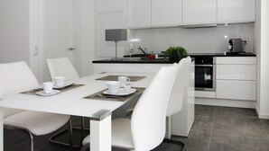 A modern kitchen with white cabinets, a built-in oven, and a dining area with white chairs and a table set for two. - Ferienhaus am Yachthafen in Peenemuende (Peenemünde)