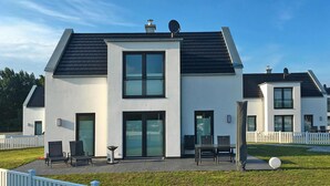 A modern two-story house with a flat roof, large windows, and a patio area with outdoor furniture. - Ferienhaus am Yachthafen in Peenemuende (Peenemünde)