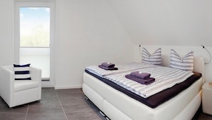 A bedroom with a bed, a chair, a bedside table, and a window. - Ferienhaus am Yachthafen in Peenemuende (Peenemünde)