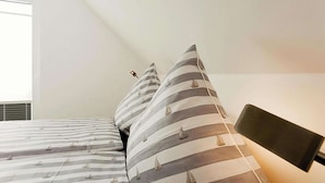 Ein Schlafzimmer mit einem Bett, gestreifte Kissen, einem Kopfteil und einem Fenster.