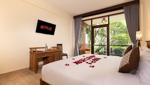 A hotel room with a bed, a desk, a chair, a TV displaying 'NETFLIX', and a window with curtains. - Umah Temuku Ubud (Ubud)