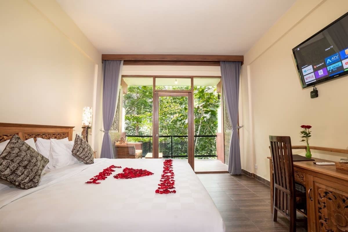 A hotel room with a bed, a desk, a TV, and a balcony with curtains.