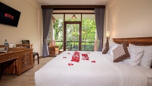 A hotel room with a large bed, a wooden desk, a television, and a window with curtains. - Umah Temuku Ubud (Ubud)
