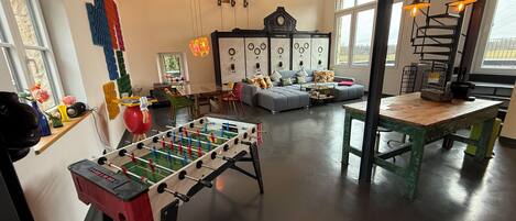 A living room with a foosball table, a sofa, a dining table, and a kitchen area.