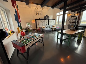 A living room with a foosball table, a sofa, a dining table, and a kitchen area.