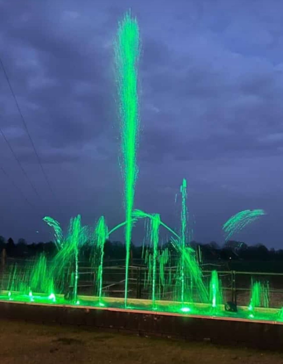 Een fontein met meerdere waterstralen, verlicht in groen.