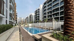 En moderne lejlighedskompoleks med swimmingpool, udendørs møbler og en palme.