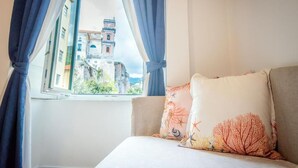 A bedroom with a bed, a window with curtains, and a view of a building with a tower. - CVM Mare Luna Guesthouse (Maiori)