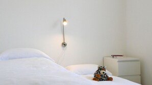 A simple room with a bed, a nightstand, a wall-mounted lamp, and a stuffed toy.
