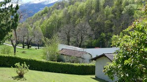 A rural landscape with a small building, a well-maintained lawn, and a forested hill in the background.