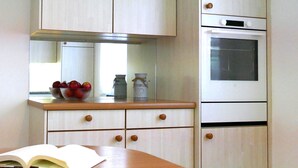 A kitchen with light wooden cabinets, a white oven, and a bowl of fruit on the counter.