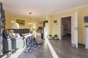 Ein modernes Wohnzimmer mit einer Couch, einem Couchtisch und einem Fernseher. Es gibt einen Essbereich mit Tisch und Stühlen sowie eine Küchenzeile mit Schränken und einem Kühlschrank.