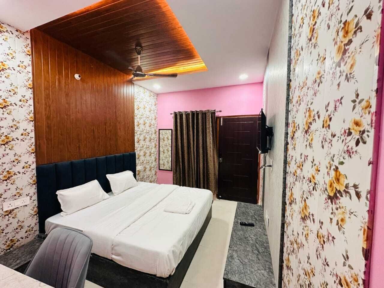 A hotel room with a bed, a desk, a chair, a ceiling fan, and floral wallpaper.