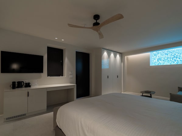 A modern bedroom with a large bed, a built-in desk, a ceiling fan, and a TV mounted on the wall. - VE ZO Suites Mykonos (Mykonos)
