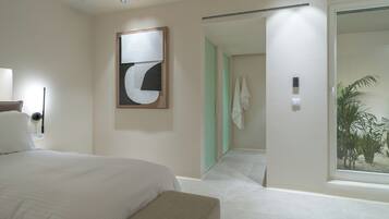 Een moderne hotelkamer met een groot bed, een wanddecoratie met abstracte kunst, een badkamer met een grote spiegel en uitzicht op een palmboom door het raam.
