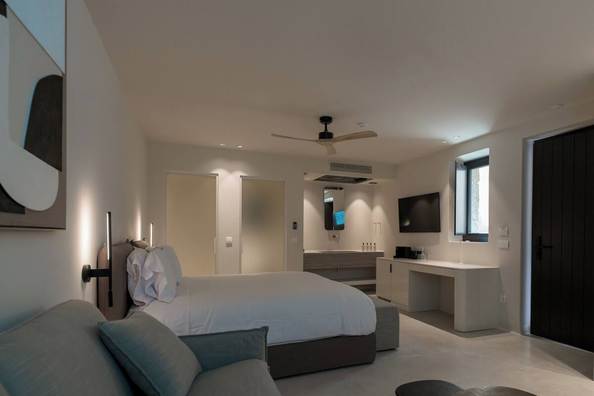 A modern bedroom with a bed, a desk, a TV, and a ceiling fan.