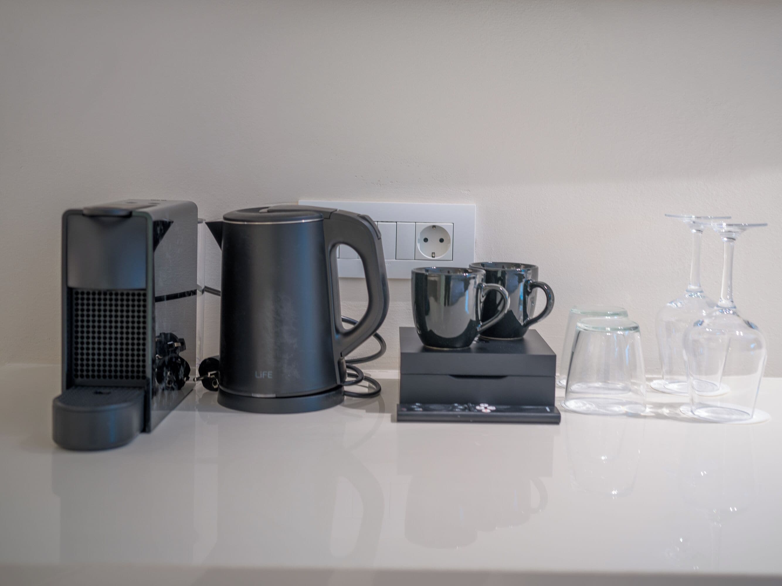 Una encimera de cocina con una cafetera, un hervidor, dos tazas y un juego de copas de vino.