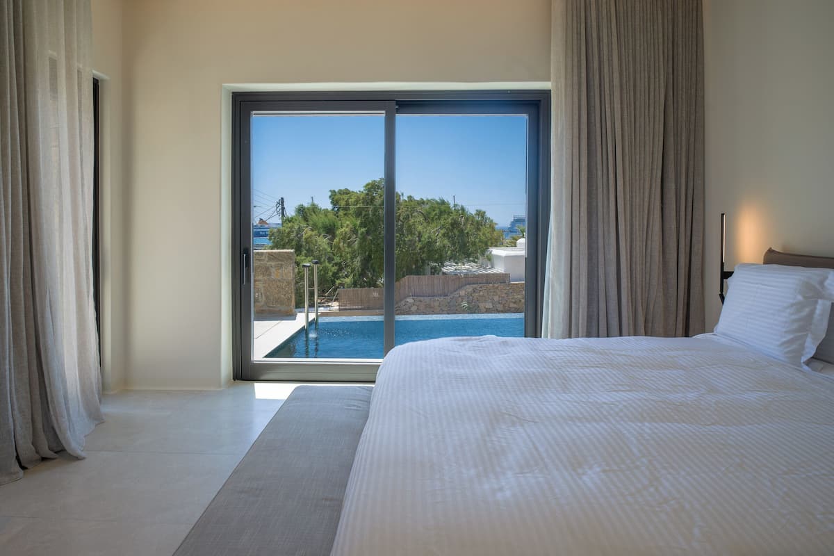 A bedroom with a large bed, a view of a swimming pool, and a sliding glass door.