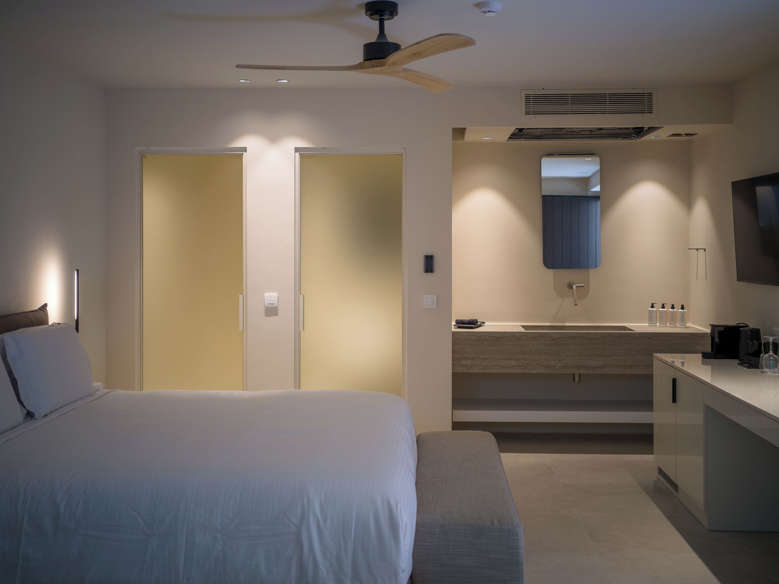 Ein Hotelzimmer mit Bett, Schreibtisch, Spiegel und Deckenventilator.