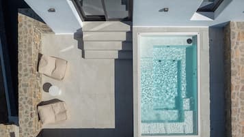 Une piscine sur le toit, bordée d’un mur en pierre, un espace détente avec des coussins et un jacuzzi protégé par des parois en verre.