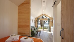 Une chambre avec un lit, deux serviettes, un mur en bois, une porte et une vue sur un espace extérieur comprenant une table et une chaise.