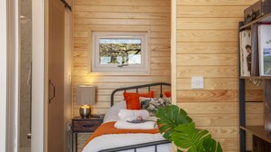 Une pièce aux murs lambrissés, avec un lit, une fenêtre donnant sur un beau paysage, une table de chevet avec une lampe et une étagère remplie de livres.