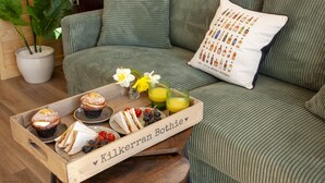 Un plateau en bois contenant de la nourriture et des boissons, posé sur un canapé vert agrémenté d’un coussin décoratif.