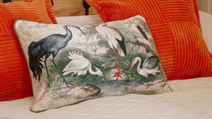 Un lit avec un drap blanc et deux oreillers orange, dont l’un est orné d’un motif représentant un oiseau et une plante.