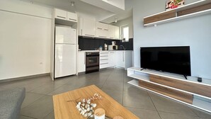 Een moderne keuken met witte kasten, een zwarte televisie en een houten salontafel.