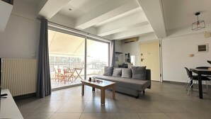 Een ruime woonkamer met een bank, salontafel en een eettafel met stoelen. Een grote schuifglazen deur leidt naar een terras.