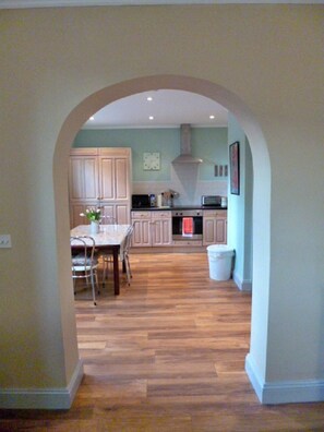 An interior view of a kitchen with wooden flooring, a dining table with chairs, and light-colored cabinets.