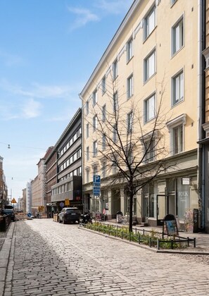 Une rue pavée bordée d’immeubles à plusieurs étages, d’un arbre et d’un panneau de signalisation de stationnement bleu.