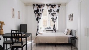Une chambre moderne avec un lit, un bureau et une chaise. On y trouve une fenêtre avec des rideaux, un radiateur et un mur décoré de tableaux.