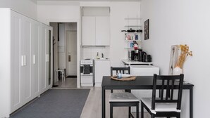 Une cuisine compacte avec des meubles blancs, une petite table à manger avec deux chaises et une machine à café.