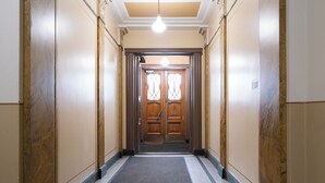 Un couloir avec une porte en bois au fond, un sol recouvert d’une moquette et un luminaire au plafond.