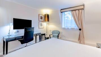 A hotel room with a large bed, a desk with a chair, a television, a lamp, and a window with curtains.