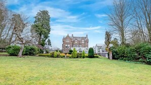 A large, historic stone building with multiple windows and a symmetrical facade, surrounded by well-maintained lawns and mature trees. - The Landmark Hotel and Leisure Club | SUPR DBL (Dundee)