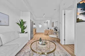 Un salón moderno con un sofá blanco, una mesa de centro redonda y una zona de comedor al fondo.