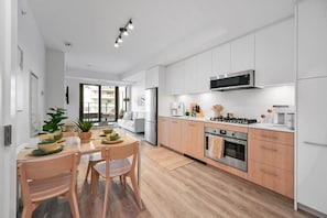 Una cocina moderna con armarios blancos, una estufa de acero inoxidable y un comedor con sillas y mesa de madera.
