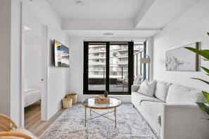 Una sala de estar moderna con un sofá, una mesa de centro y vistas a un paisaje urbano a través de grandes ventanales.