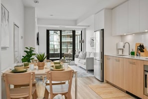 Una cocina moderna con armarios de madera, un área de comedor con una mesa para dos, y vista al salón.